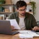 Small-business owner comparing computing costs with a laptop, paperwork and calculator.